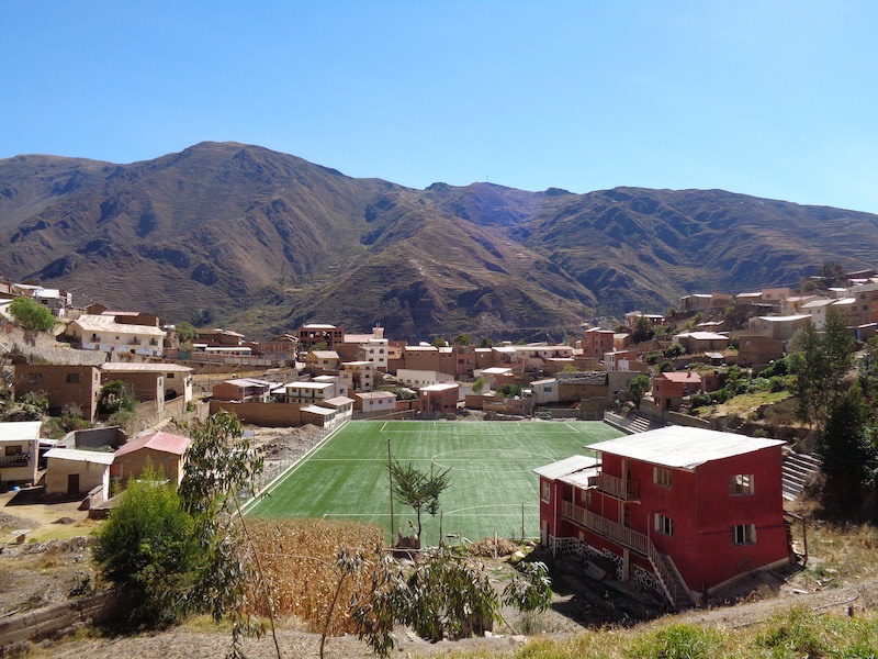 Foto van voetbalveld in een dorp met achtergrond van bergen